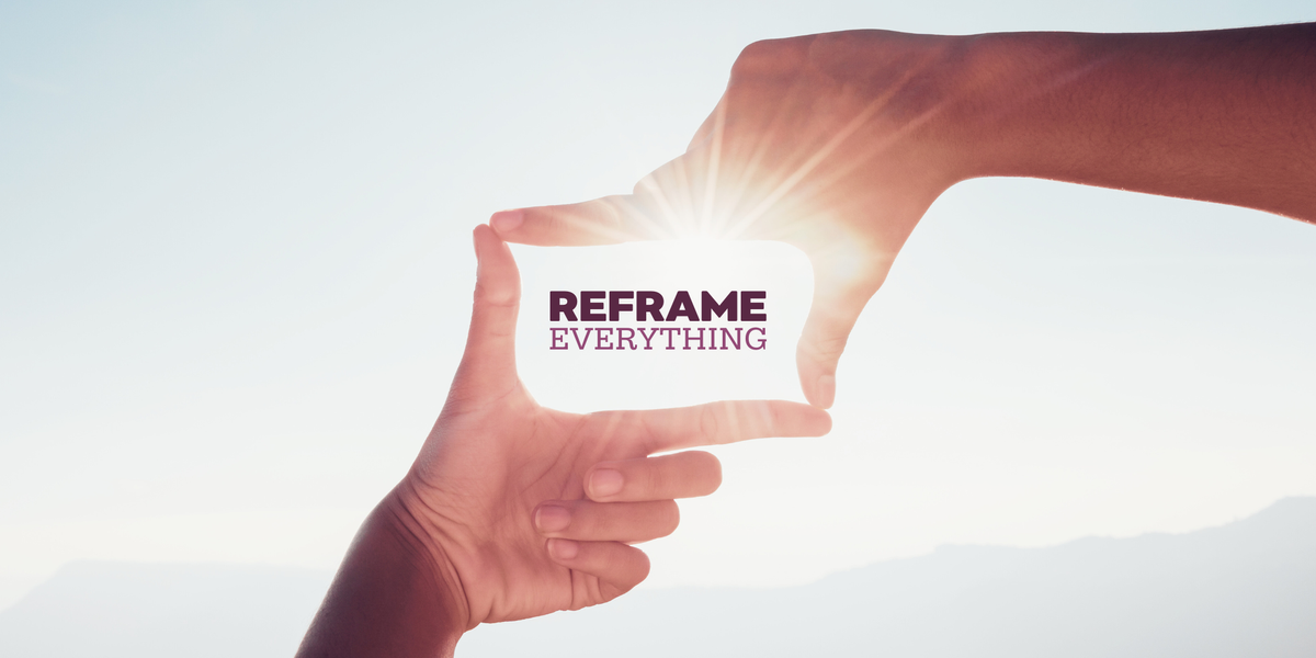 Two hands forming a frame with a solar flare behind them and distant hills. "Reframe Everything" is overlaid within the hands.